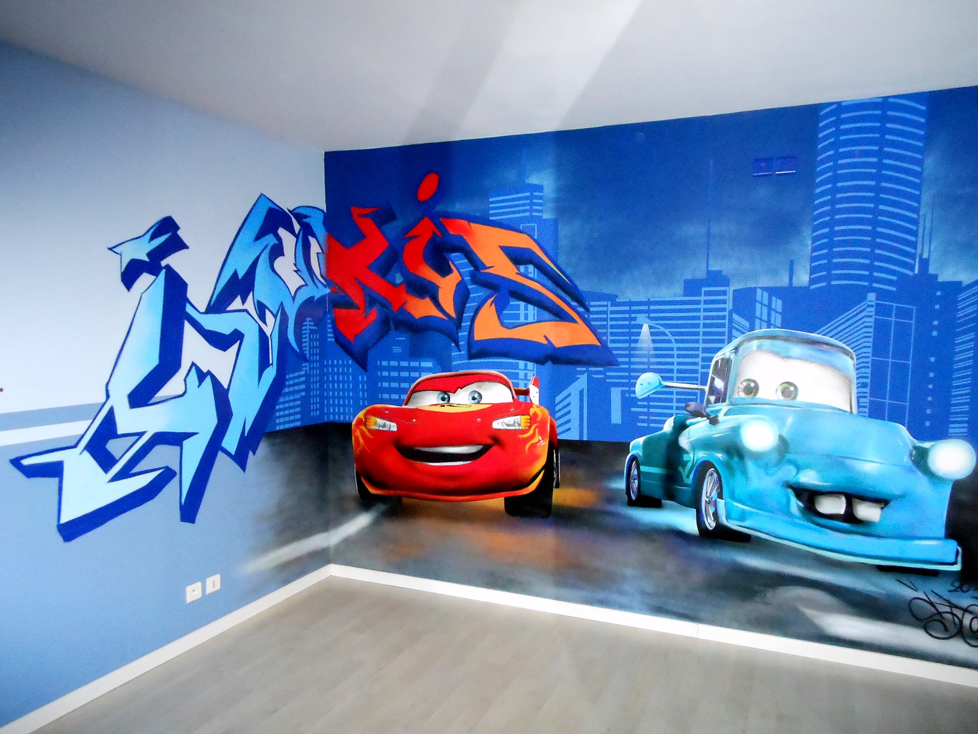 Graff peint à la bombe dans une chambre d’enfant : voiture de course rouge, dépanneuse bleue et ville de nuit