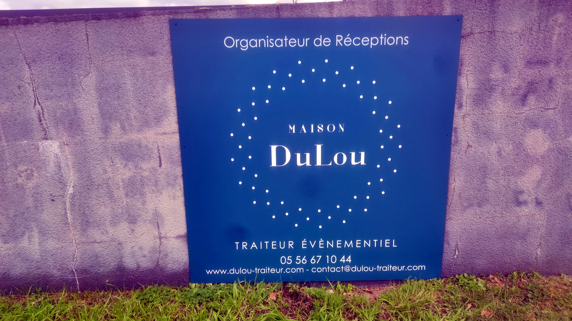 Panneau de signalétique Maison DuLou, traiteur événementiel, fixé sur un mur de clôture