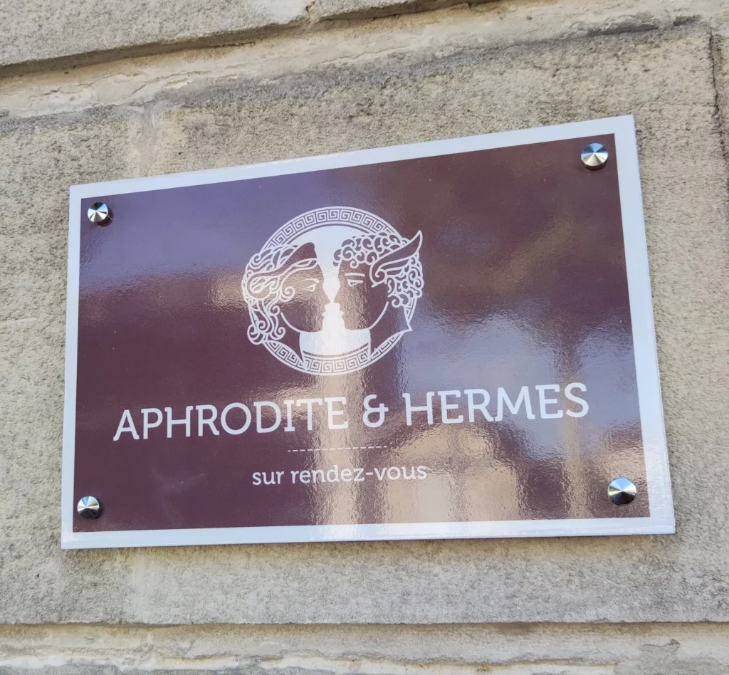 Plaque professionnelle de façade Aphrodite & Hermès fixée par entretoises sur pierre – Saintes